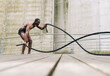 Bare chested african american man exercising with battle ropes in gym. elite athlete concept