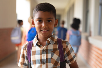 Wall Mural - Portrait of smiling biracial elementary schoolboy standing in corridor