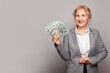 © millaf (Nemchinova) - Senior business woman showing money us dollars on gray background