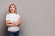 Optimistic confident senior woman wearing white t-shirt standing with crossed arms on gray studio wall background