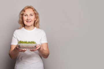 Wall Mural - Happy senior woman holding microgreen vegetarian food on gray studio wall banner background