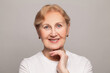 Portrait of smiling senior woman with perfect skin looking at camera on grey background. Closeup face of mature woman, skin care and anti-aging wrinkle treatment.