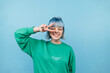 © bodnarphoto - Attractive hipster girl in casual clothes stands on a blue background and shows a gesture of peace winking.