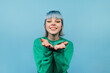 © bodnarphoto - Portrait of a joyful hipster girl with blue hair stands on a blue background with a smile on his face and shows an air kiss.