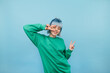 © bodnarphoto - Positive woman in green sweatshirt and with colored hair dances on a blue background with a smile on her face.