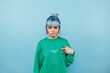 © bodnarphoto - Dissatisfied hipster girl with colored hair stands on a blue background and points a finger at himself and looks at the camera and misses