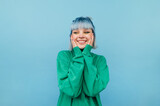 Fototapeta Uliczki - Joyful girl with blue hair stands on a green background with a smile on his face and happy looks away.