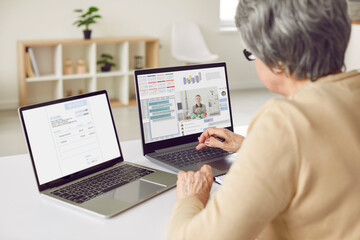 Adult woman working on two computers. Entrepreneur sitting at desk in front of two laptop screens, using lots of modern apps, taking online business consultation, getting help with electronic document