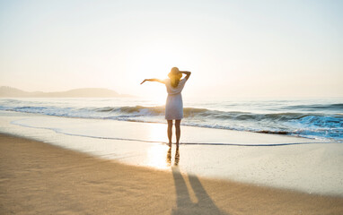 Wall Mural - Happy woman standing on the beach with arms outstretched.