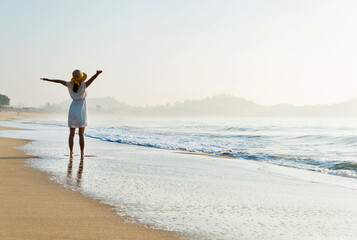 Wall Mural - Happy woman standing on the beach with hands up.