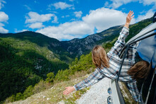 Young Carefree Woman Wearing Plaid Shirt Sticking Out Of The Window Of White Car. Free Spirited Female Enjoying Her Road Trip, Experiencing Spiritual Uplifting. Copy Space, Background, Mountain View.