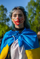 Fototapeta protest against the war in ukraine and russian invasion. portrait of a woman with ukrainian national flag and a drawn trace of a bloody hand on the face
