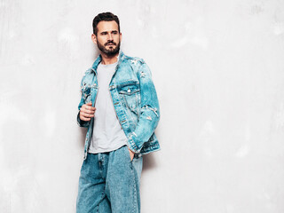 Wall Mural - Portrait of handsome confident stylish hipster lambersexual model. Sexy man dressed in jeans jacket. Fashion male isolated on grey wall in studio