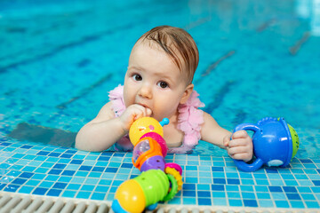 Little baby girl is playing with bright toys in the pool.