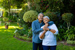 Smiling biracial senior couple embracing and looking up while standing against plants in park