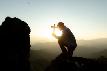 Silhouette rosary against cross in hand. Background sunrise
