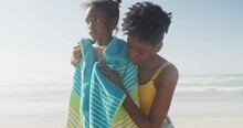 African american mother drying her daughter with a towel at the beach