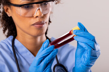 Wall Mural - African american mid adult female doctor wearing protective eyewear and gloves holding test tube