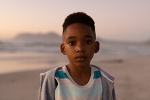 Portrait Of African American Cute Boy Wearing Jacket Standing At Beach Against Clear Sky At Sunset