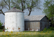 An Old Silo And Barn Sit In A Field With Wildflowers.