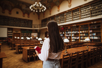 Back of female student in university campus library with book in hand. Studying in library.