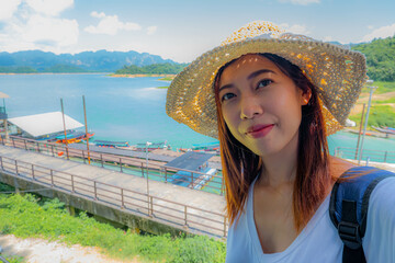 happy young woman tourist in asian hat on lake and mountain vacation smiling at camera taking photo 