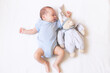 The baby is lying in a crib with a teddy bear . The baby is 0-3 months old. A calm sleeping baby. Healthy baby sleep. An article about toys for kids. A soft toy.