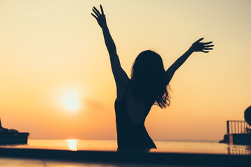 silhouette of woman in the pool water on summer vacation with sunset view.