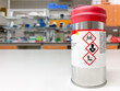 Can with extremely dangerous substance inside, labelled with symbols indicating that the content is toxic. Laboratory space is visible in the background.