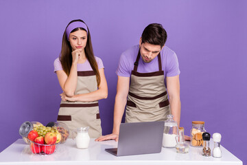 Canvas Print - Photo of cute thoughtful boyfriend girlfriend dressed chef outfits reading recipes modern gadget isolated purple color background