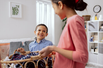 Wall Mural - Siblings stand in the middle of the laundry room holding a bowl of clothes near the washing machine, children are wearing comfortable clothes smile shared childhood.