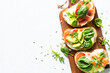 Open sandwich set with cream cheese, prosciutto, salmon, avocado and fresh greens. Top view at white table. Close up.