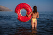 slender woman with a sexy booty in a swimsuit holds an inflatable circle in hands on sunny summer day at sea on vacation
