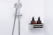 Shower head and  bathroom shelf with toiletries on background of white wall with metro ceramic tiles.
