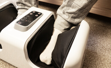 Foot massager. A man relaxes during a foot massage at home. Close-up of an electric massager device.