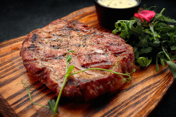 Pork neck steak with sauce and arugula, on a wooden board