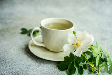 Cup Of Green Tea Next To White Wild Roses On A Table