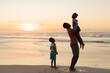 © WavebreakMediaMicro - African american son looking at father picking up girl while standing on beach against sky at sunset