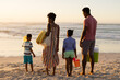 © WavebreakMediaMicro - Rear view of african american young parents and children with cooler, blanket and pail at beach