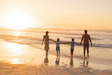 Rear view of african american young parents holding son and daughter's hands at beach against sky