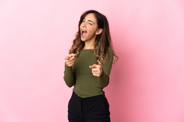 Wall Mural - Young caucasian woman isolated on pink background pointing to the front and smiling