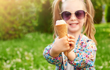 Close-up ice cream in a waffle cone in the hand with. Cheerful smiling child is holding it on summer green lawn background. Vacation and summer time concept