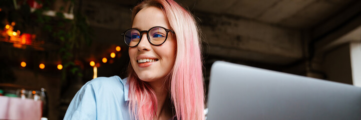 Wall Mural - Young smiling woman working with laptop while sitting in cafe