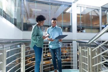 Smiling african american male and female professionals discussing over file on staircase