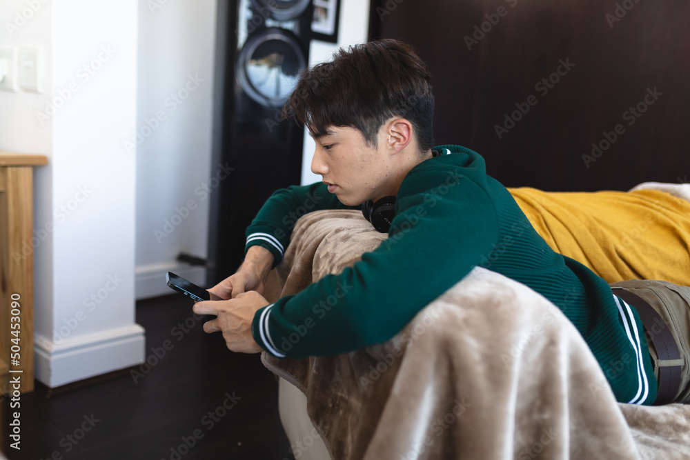 Side view of asian teenage boy using smartphone while lying on front ...