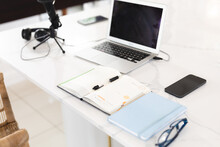 High Angle View Of Laptop, Mobile Phone, Microphone, Diaries With Pen And Eyeglasses On Table