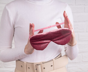 A girl in light clothes holds a pink sleep mask on a light background with copy space. The concept of eye protection from light for good sleep and melatonin production, tranquility.