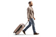 Full length profile shot of a man walking and pulling a suitcase