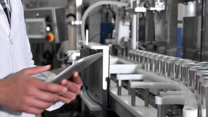 Wall Mural - Male worker types on a tablet near conveyor with cans at beverage factory production line, close up. High quality 4k footage