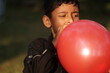 © Dream Lover/Stocksy - A little boy blowing a red balloon at outdoors in daytime